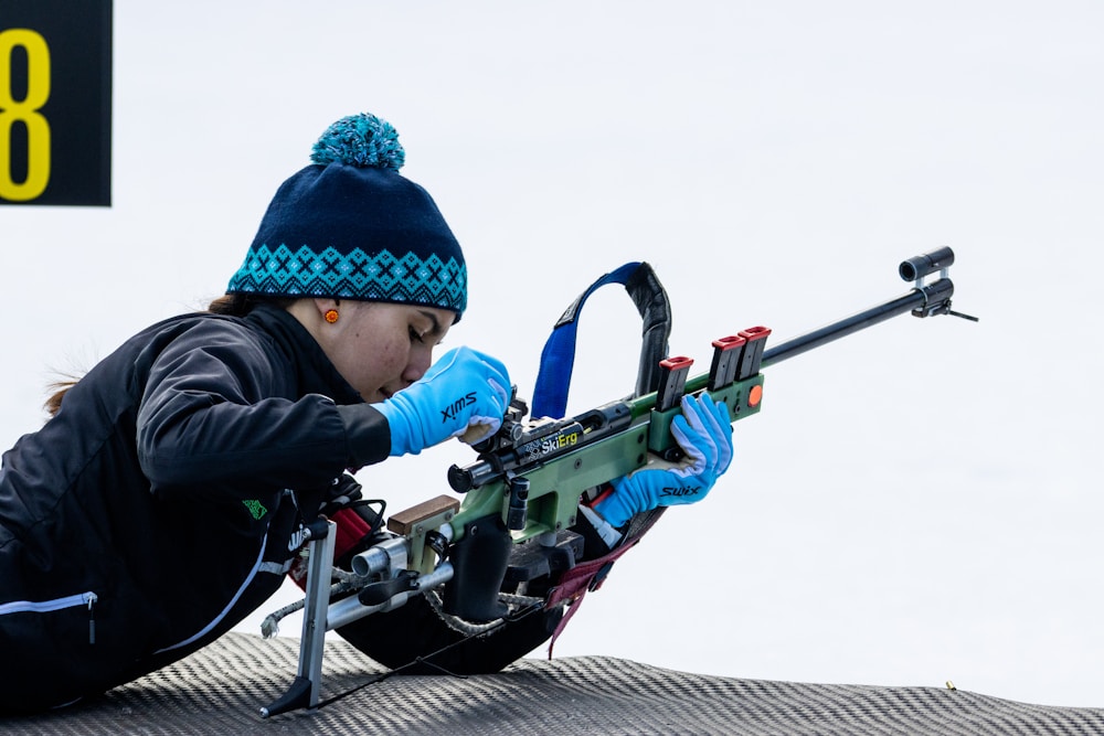 a woman with a hat and gloves is aiming a rifle, Giochi Paralimpici Milano Cortina 2026