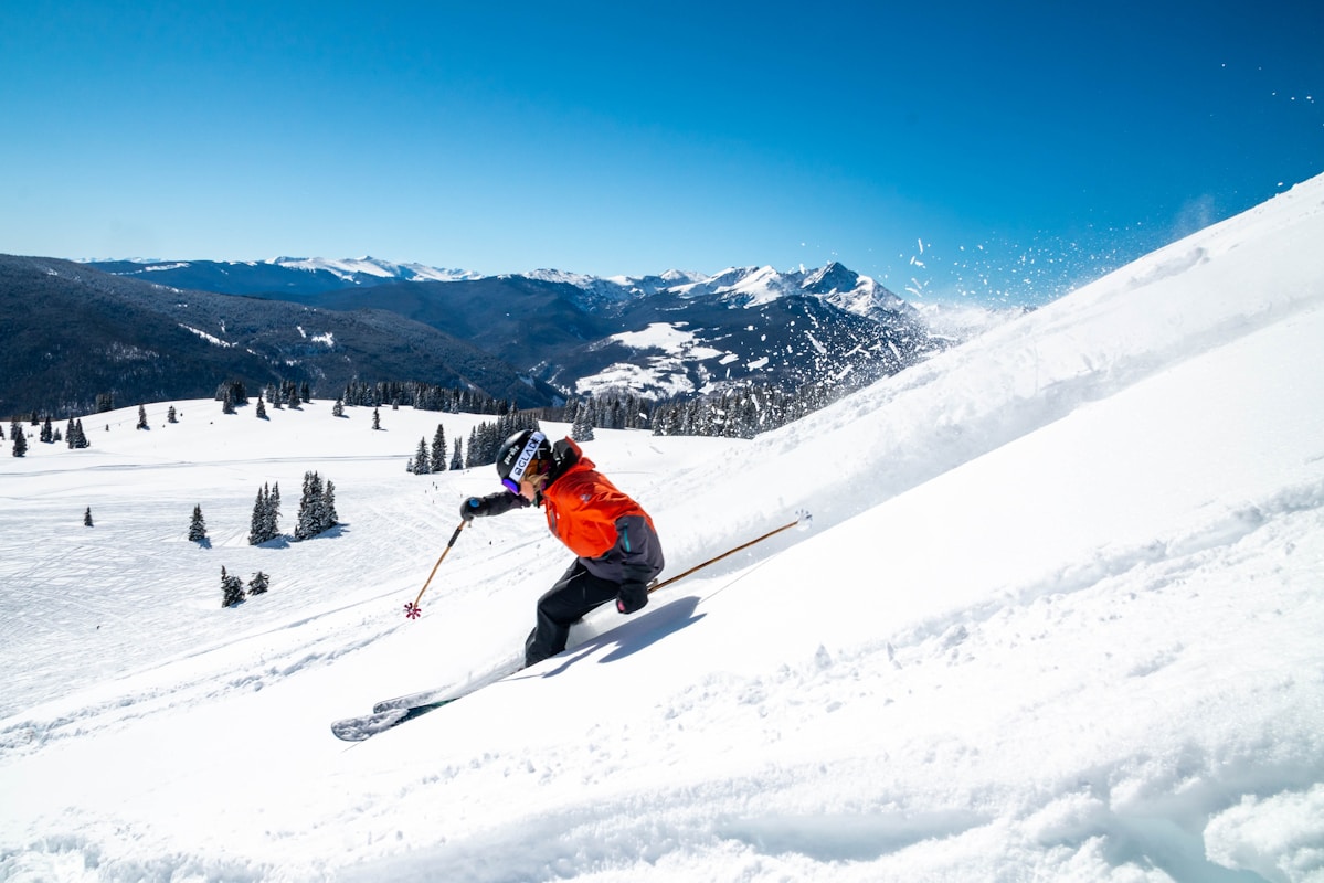 person in orange jacket and black pants riding ski blades on snow covered mountain during daytime sci di fondo vicino Milano