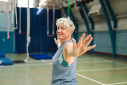 Elderly woman smiling and extending arms in gym corsi ginnastica dolce anziani Milano