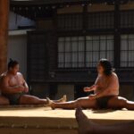 A group of people sitting on the ground in front of a building sumo e benessere fisico