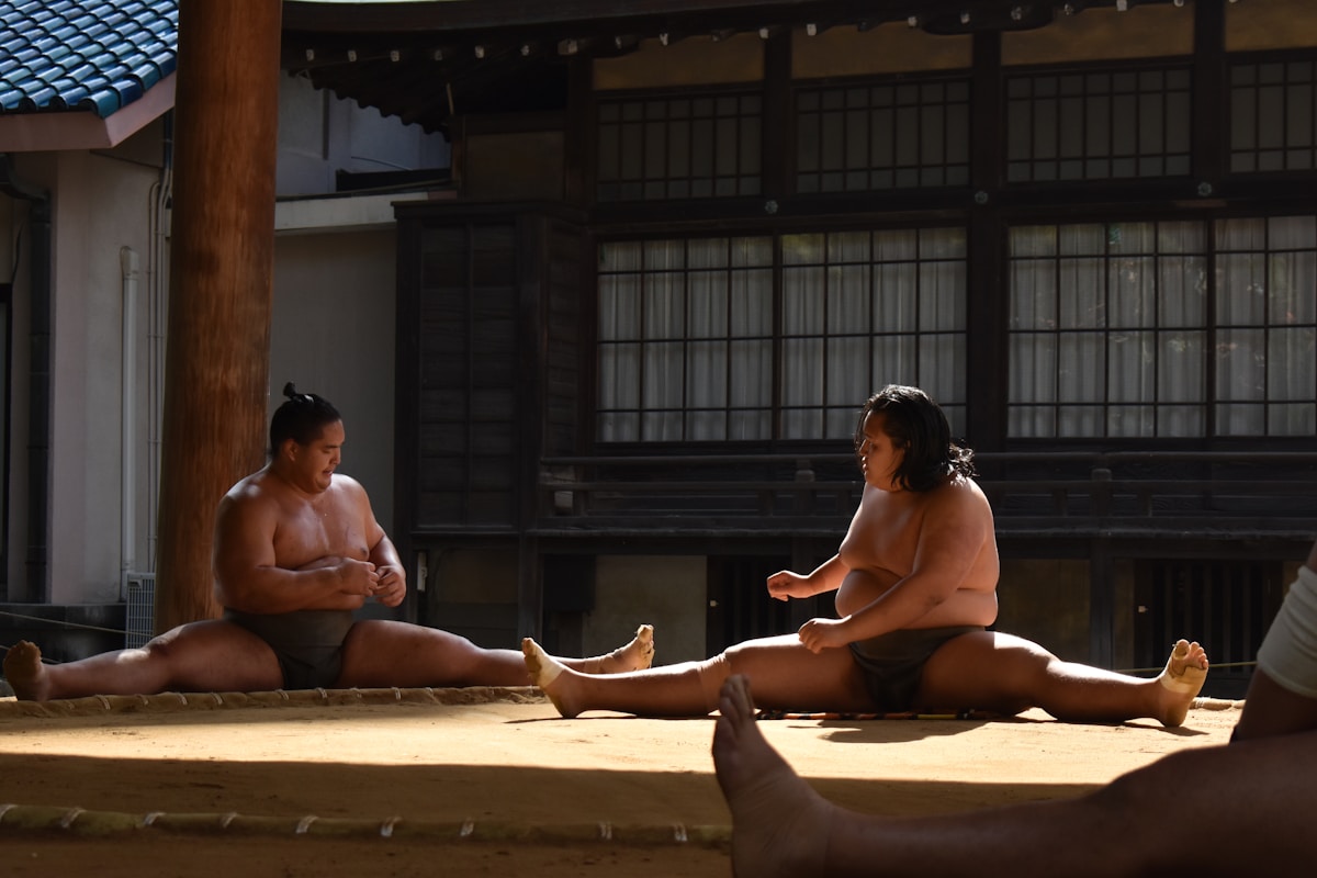 A group of people sitting on the ground in front of a building sumo e benessere fisico