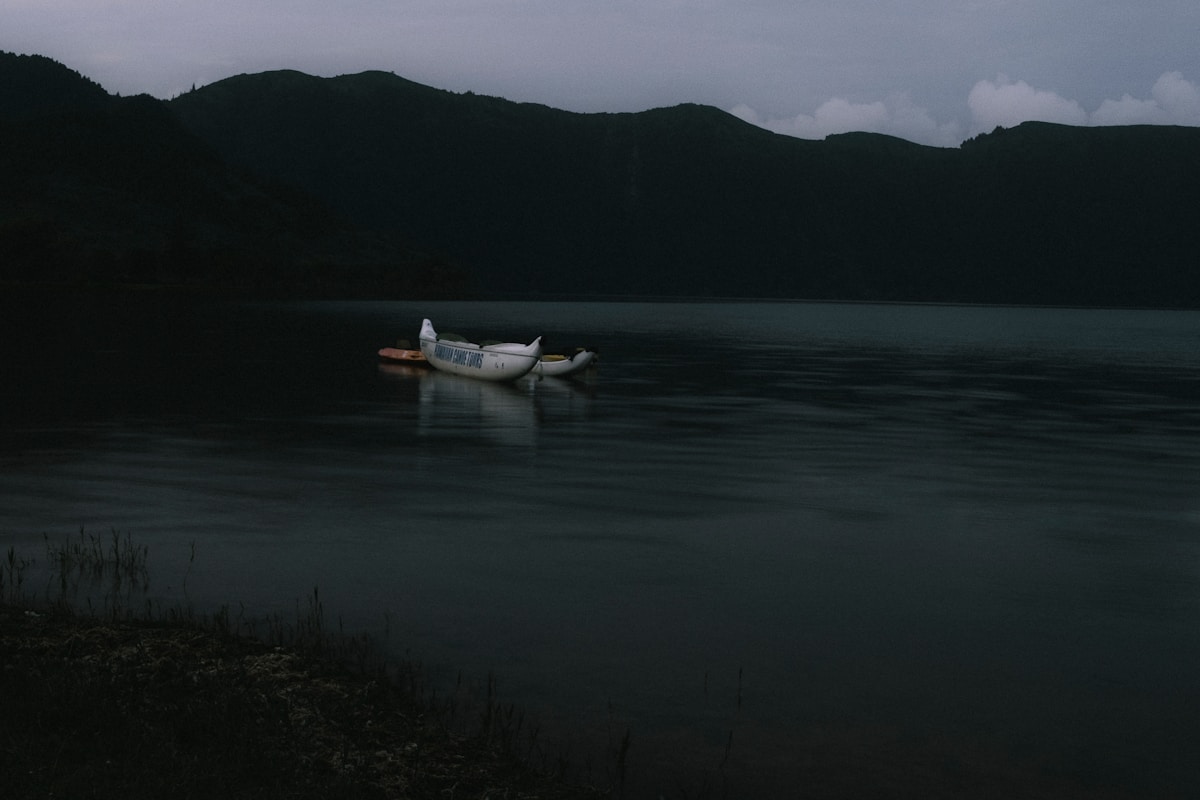 A small boat floats on a dark lake at dusk.