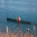 woman in black and red dress sitting on black boat on sea during daytime canoa a Milano